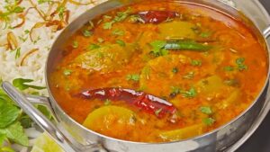 A bowl of Veg Dalcha, a South Indian lentil and vegetable stew, garnished with fresh coriander, served with rice on the side.